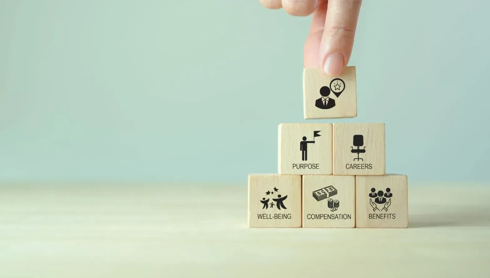 Hand stacking wooden blocks labeled with workplace benefits such as purpose, careers, and well-being