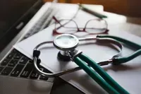 Stethoscope resting on a laptop keyboard with reading glasses
