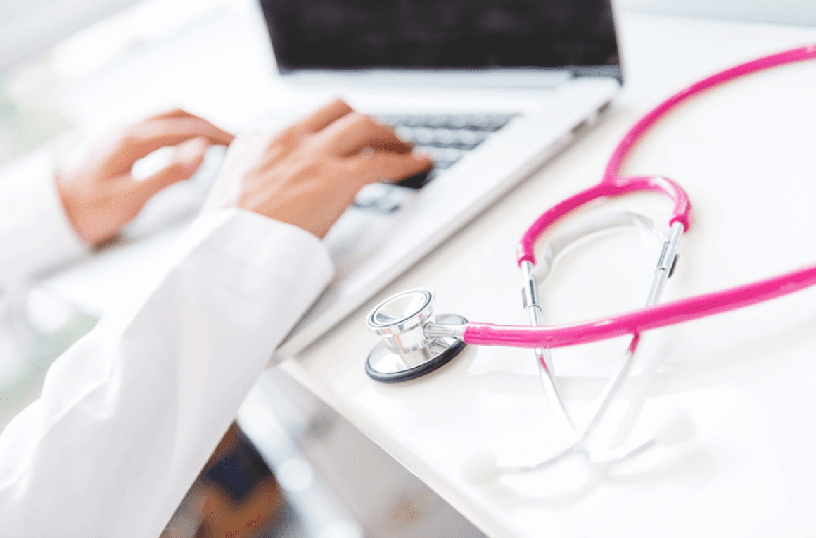 Physician typing on a laptop beside a stethoscope