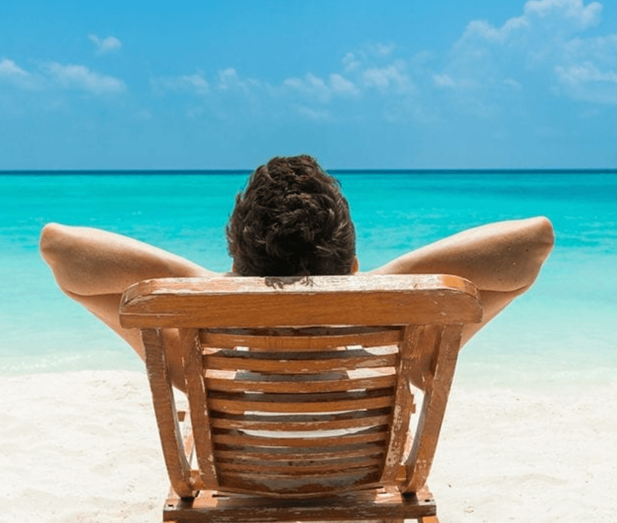 Man relaxing in a wooden beach chair facing the ocean
